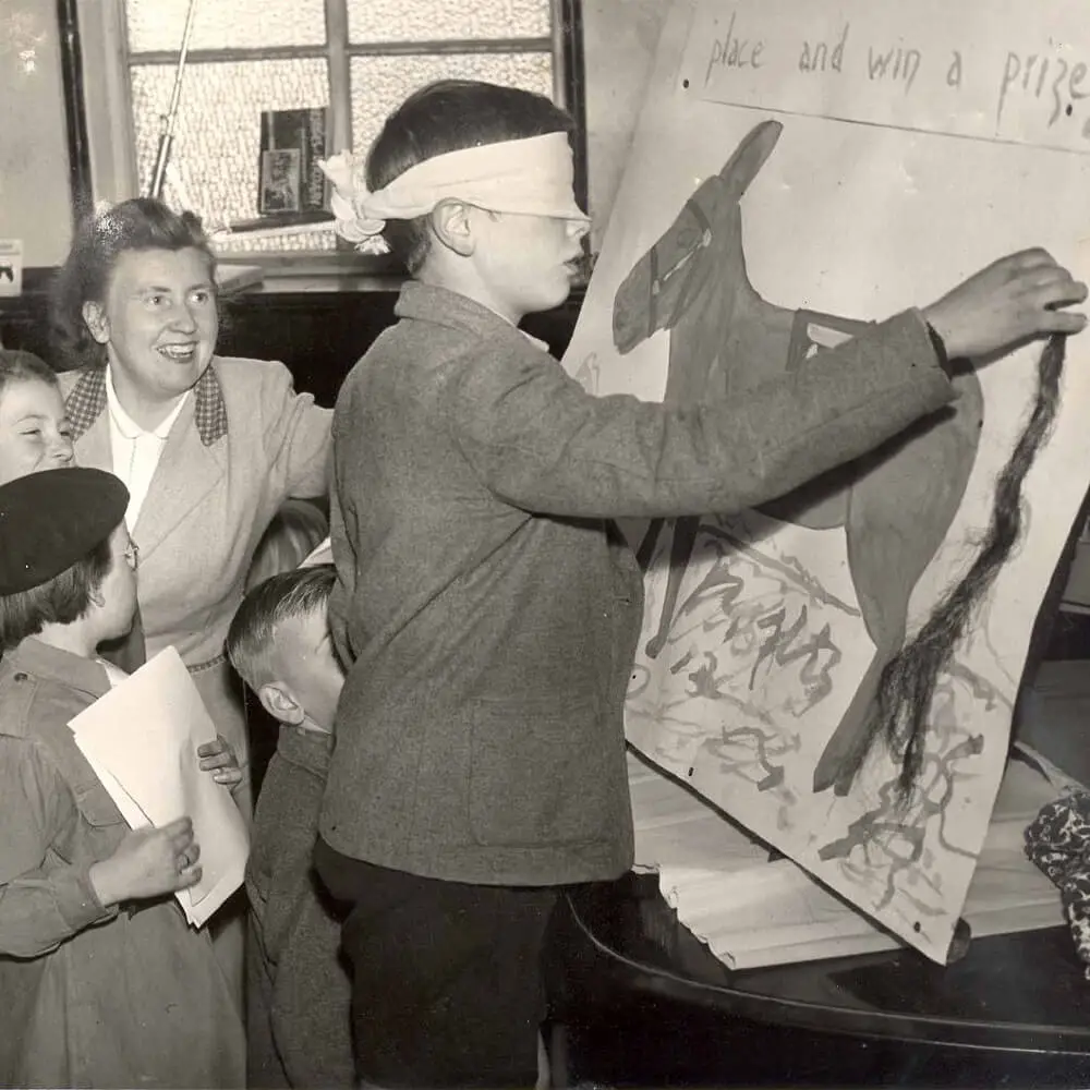 Vintage 1960s party game showing a blindfolded boy playing pin the tail on the donkey.