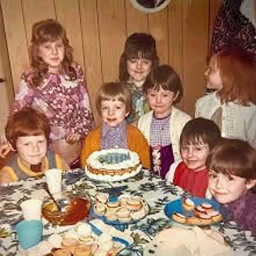 Vintage 1970s children's birthday party showing a group of kids sitting around a traditional tea table with a cake.