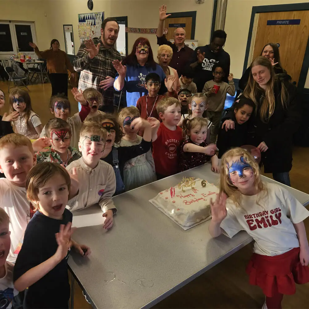 Music and Mayhem children's entertainer hosting Emily's 6th birthday party with a large group of children wearing face paint gathering around the cake.