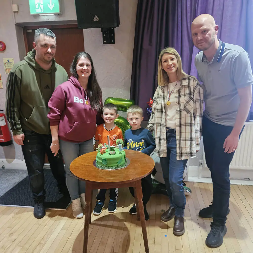 Music and Mayhem children's entertainer hosting Josh and Jack's joint 5th birthday party with a dinosaur-themed cake.