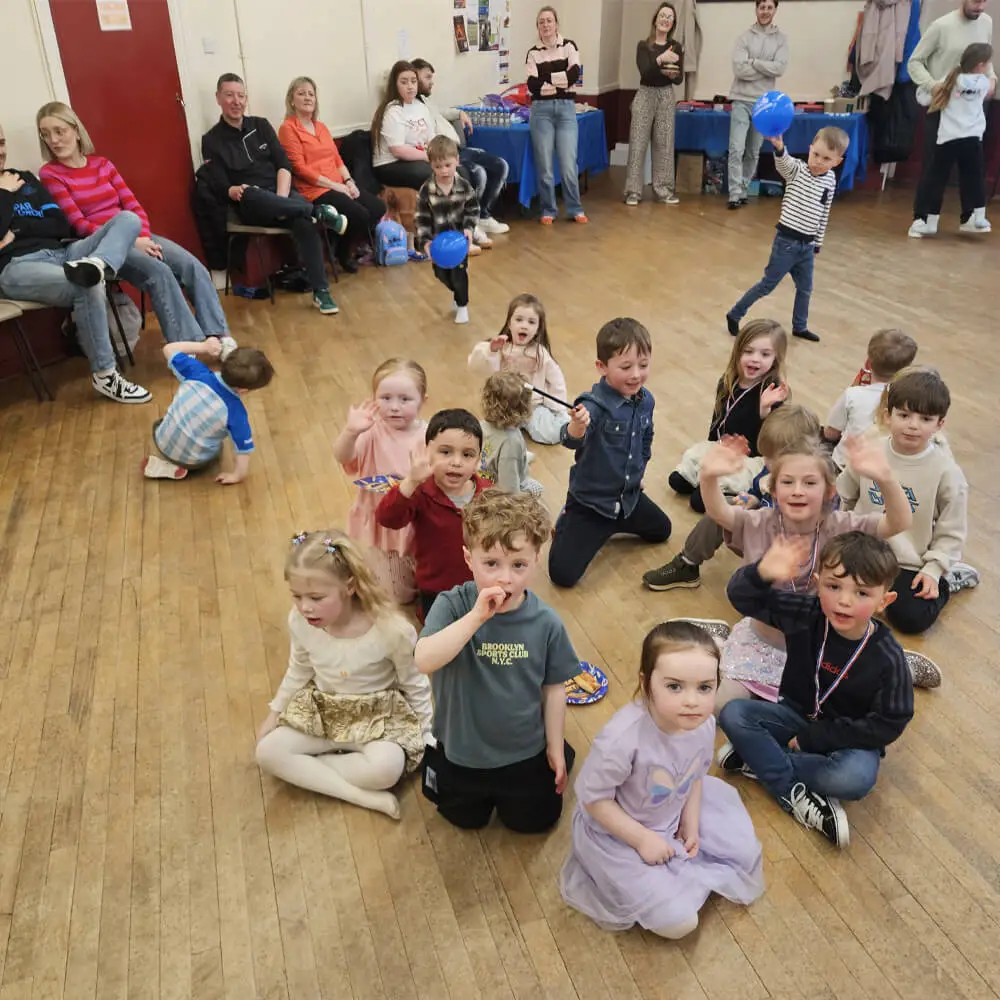 Music and Mayhem children's entertainer engaging a group of kids sitting on a village hall floor during a birthday party.