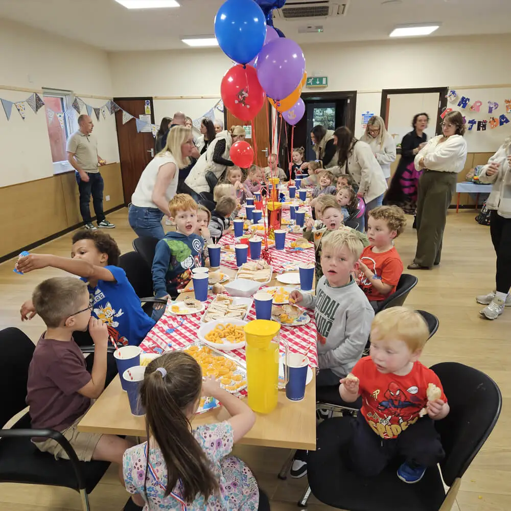 Children sitting at a long table eating party food during a Music and Mayhem birthday event.